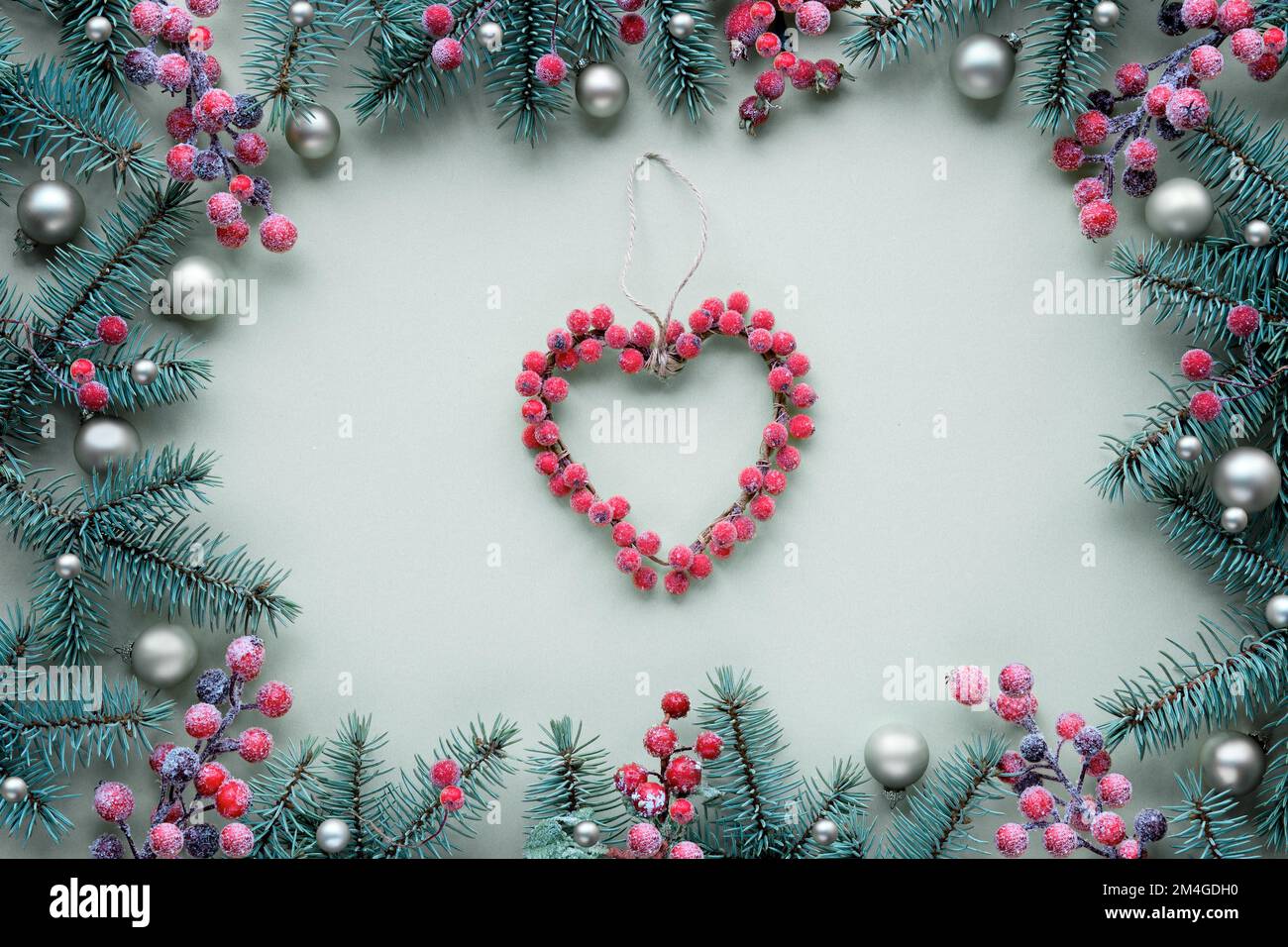 Christmas heart wreath made of berries. Frame with fir twigs and golden baubles, trinkets. Top view, flat lay, festive Xmas background on light mint Stock Photo