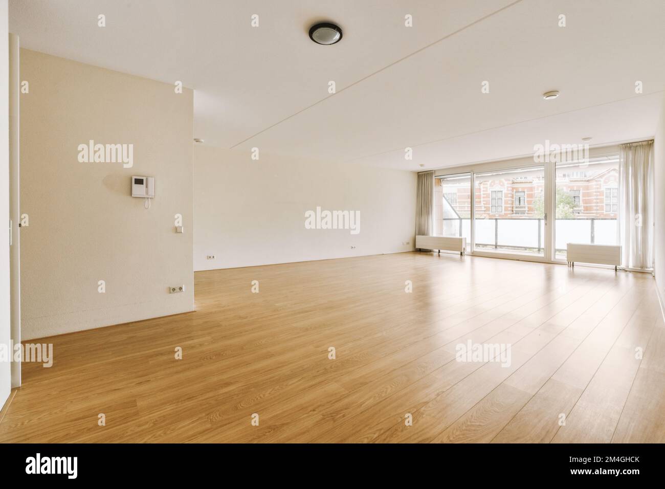 an empty living room with wood flooring and large windows looking out