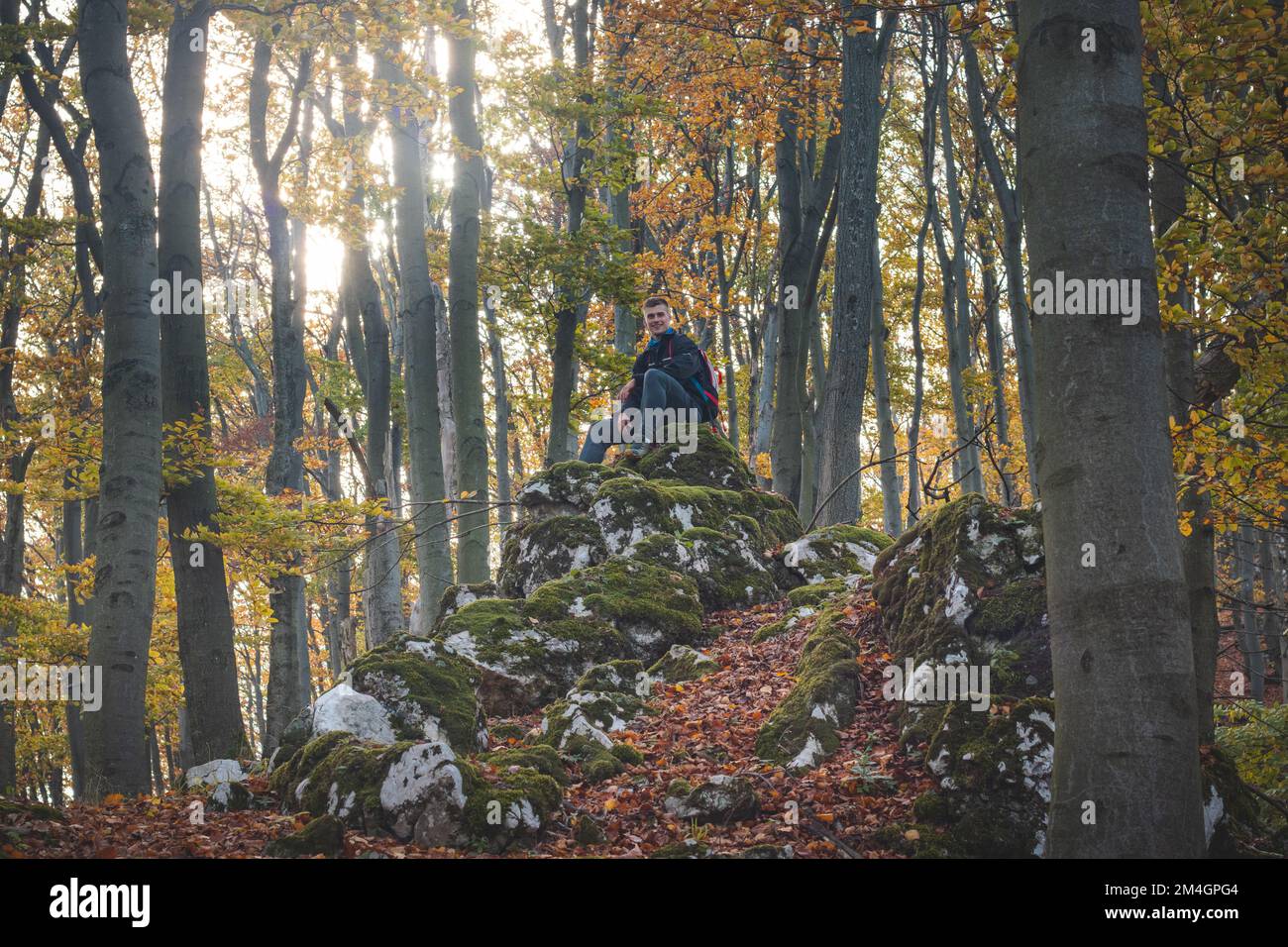 Adventurer sitting on a rock in autumn forest in Strazovske mountains, Slovakia. A man with a smile rests after a hard hike. Stock Photo