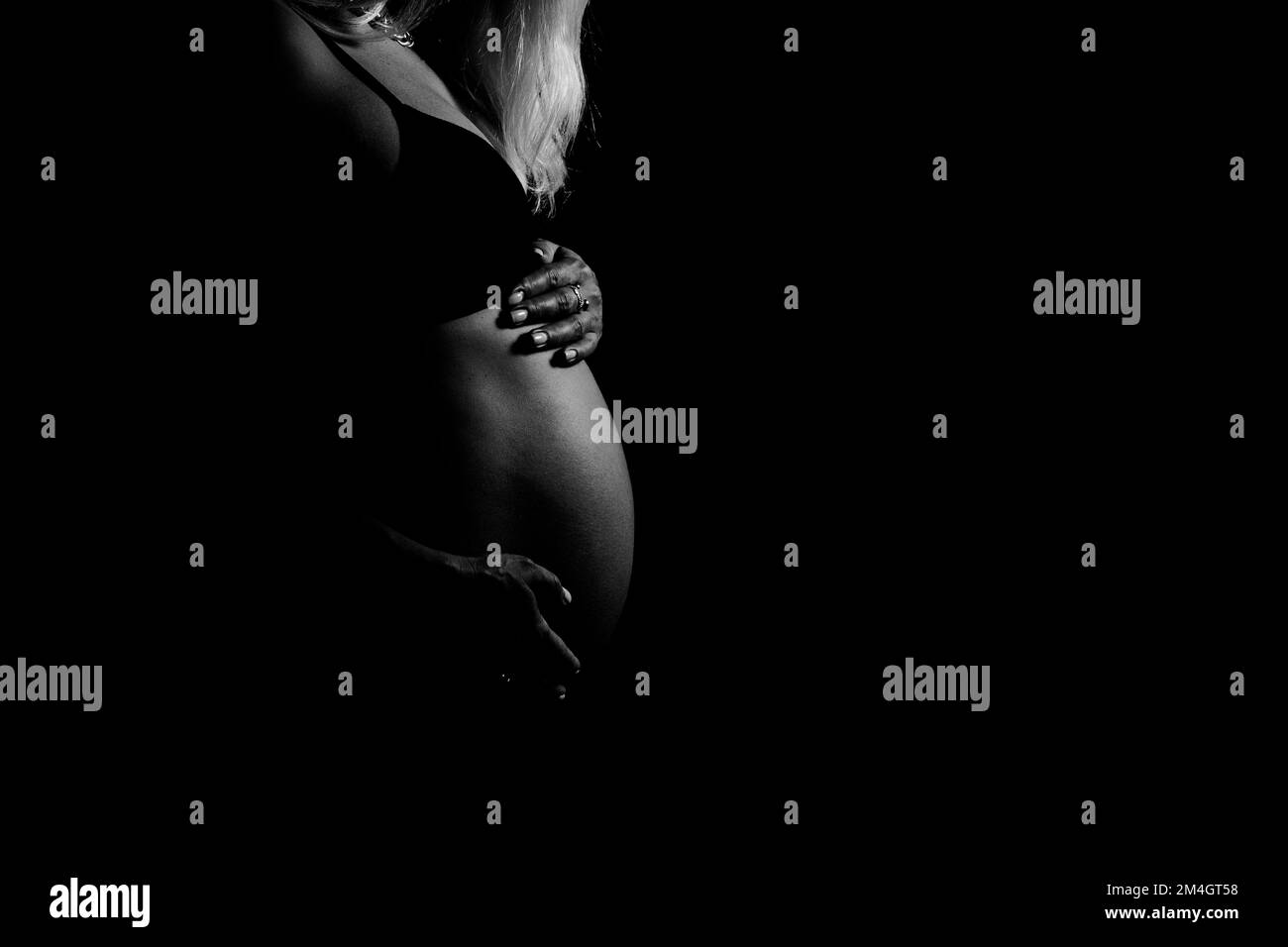 Black and white view of pregnant woman touching her belly. Pregnancy, maternity, preparation and expectation concept. Stock Photo