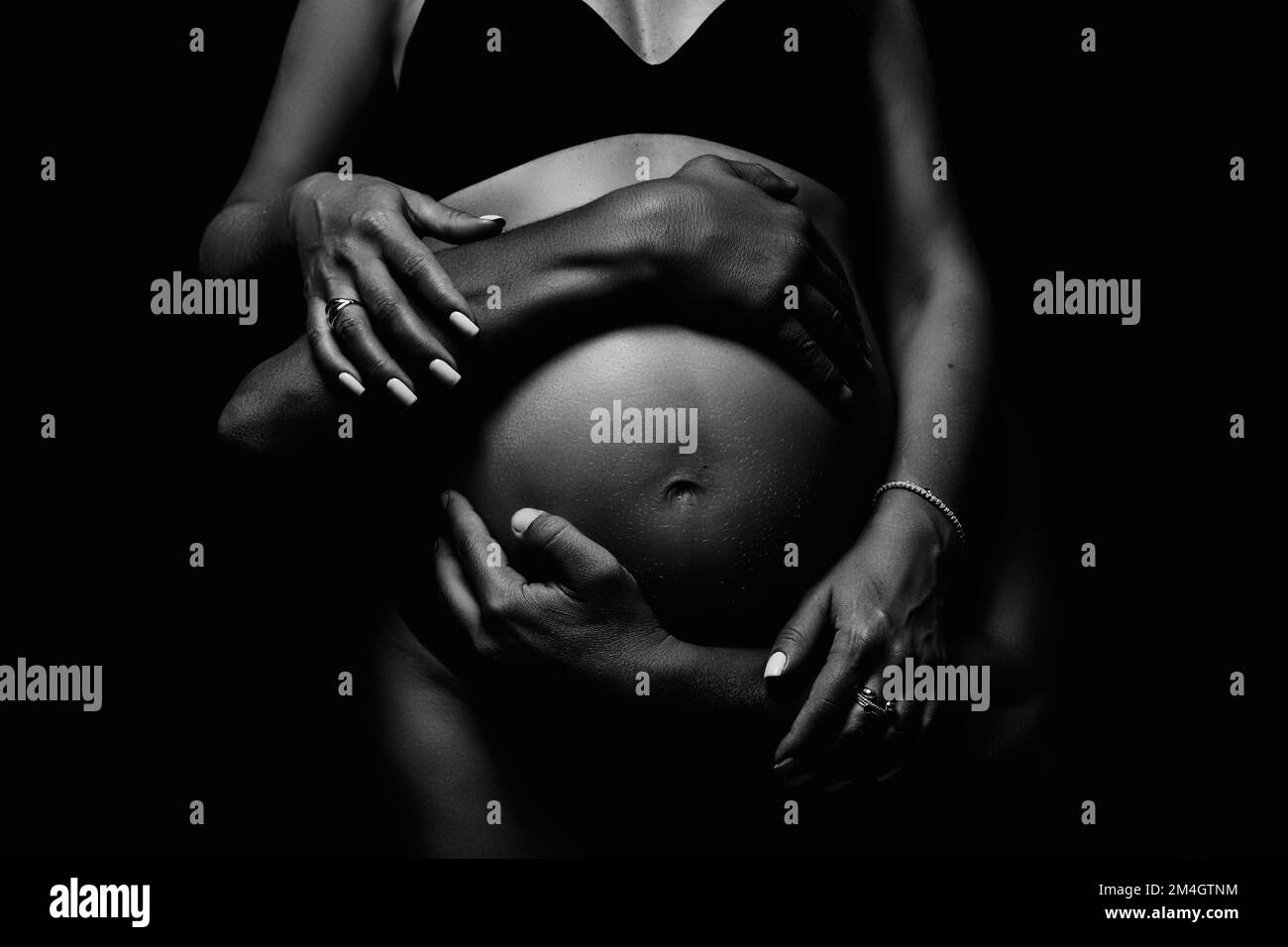 Male and female hands hug the belly of a pregnant woman. Black and white shooting. Stock Photo