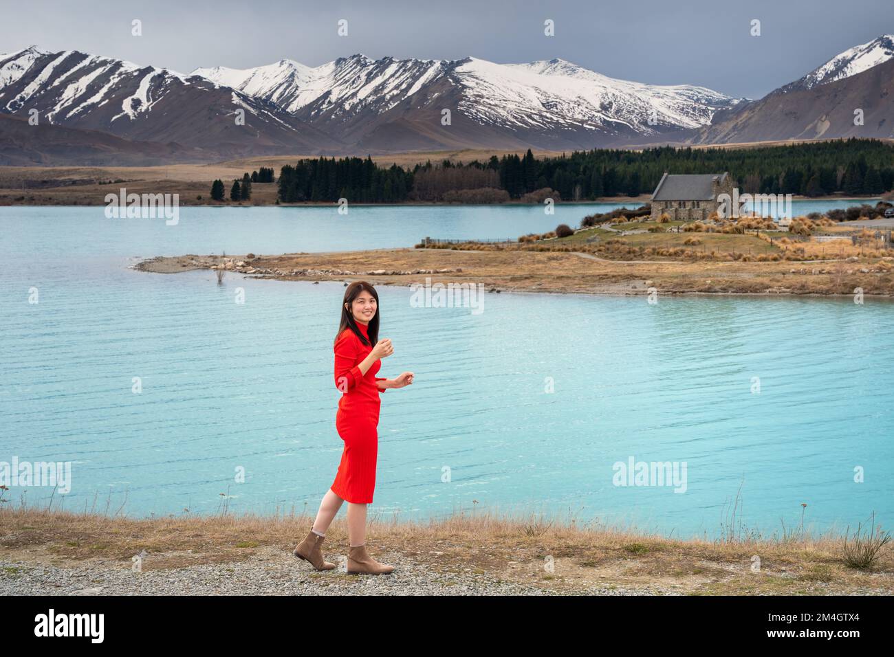 Asian female tourist pose at turquoise color Lake Tekapo with snow capped New Zealand southern alps at the background. Stock Photo