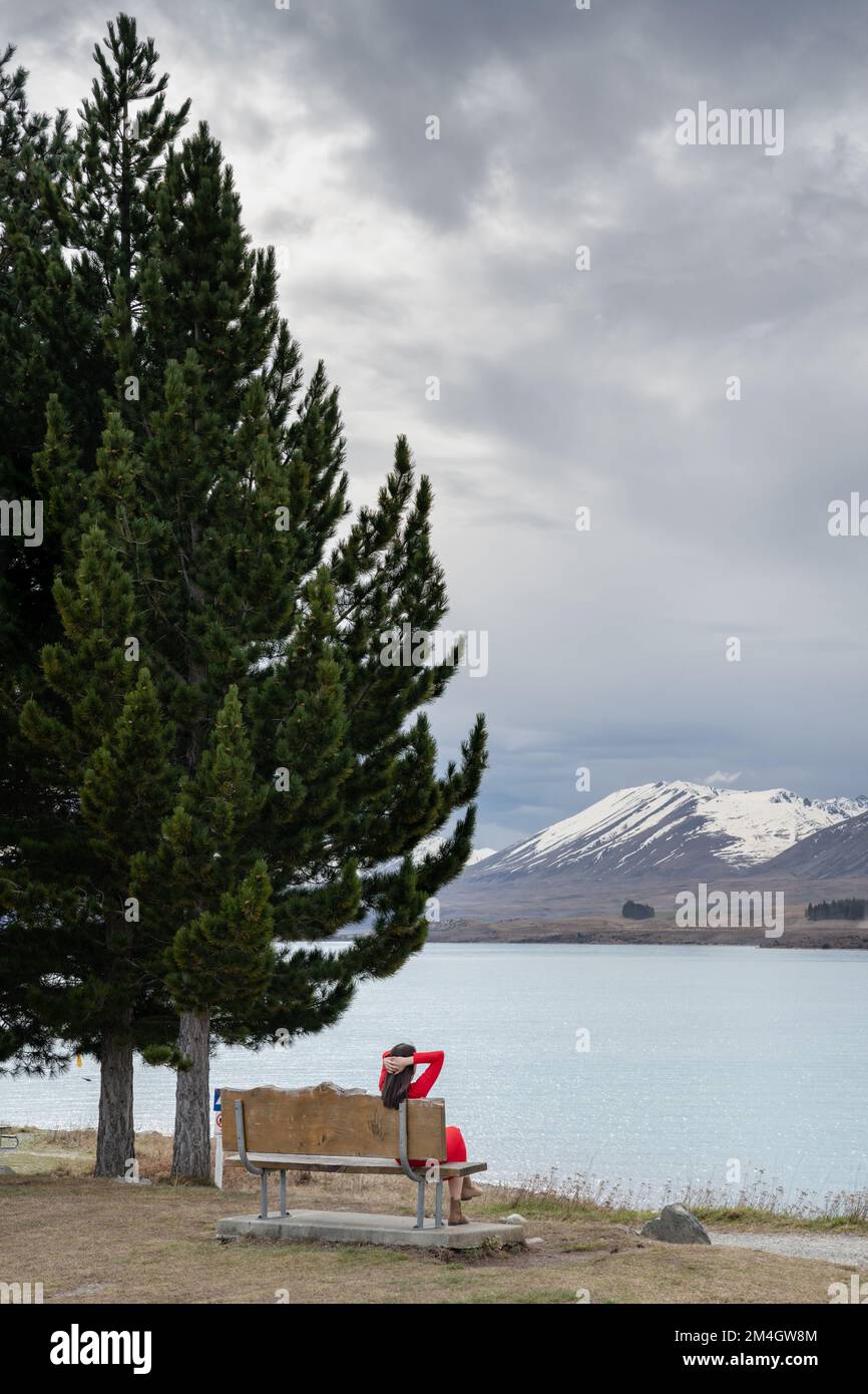 Asian female tourist pose at turquoise color Lake Tekapo with snow capped New Zealand southern alps at the background. Stock Photo