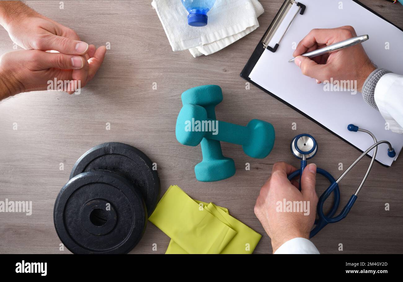 Physiotherapist doctor with patient taking notes on consultation table with medical control and sports equipment. Top view. Stock Photo