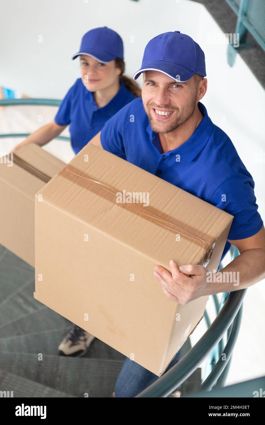 two young movers in uniform carrying parcels on staircase Stock Photo