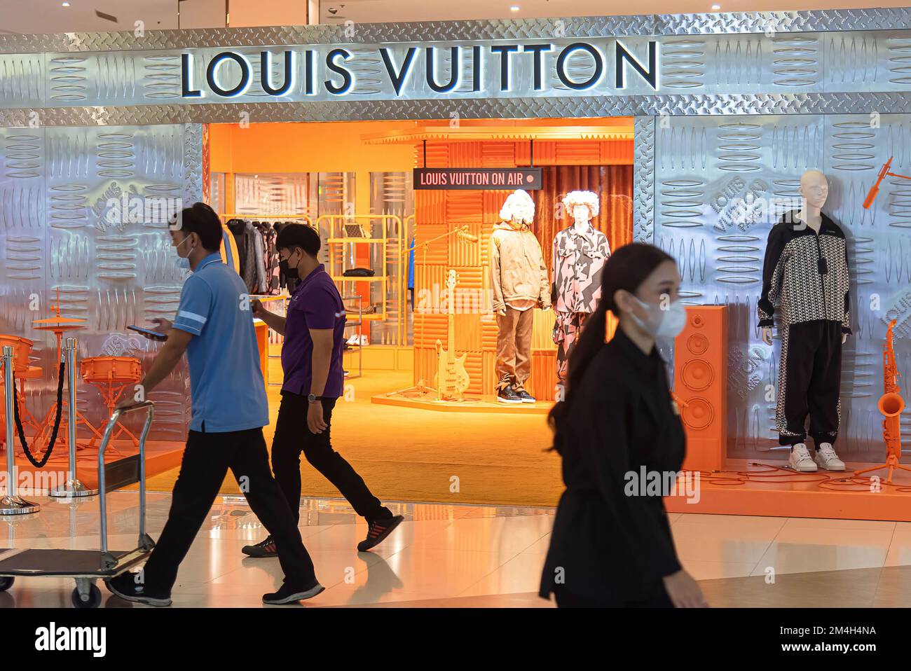 People walk past a Louis Vuitton store at Siam Paragon shopping