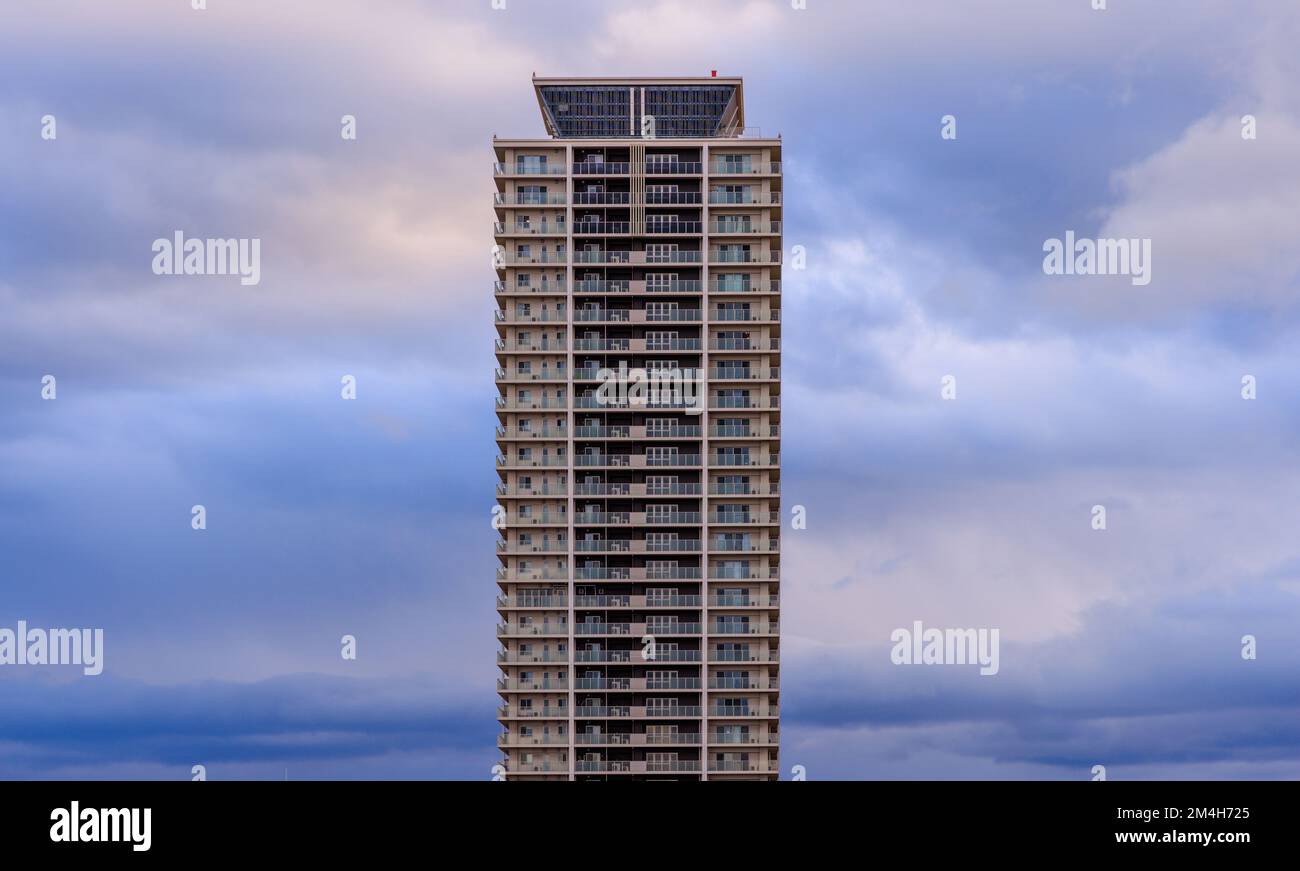 Tall residential apartment building and fluffy clouds in blue hour Stock Photo