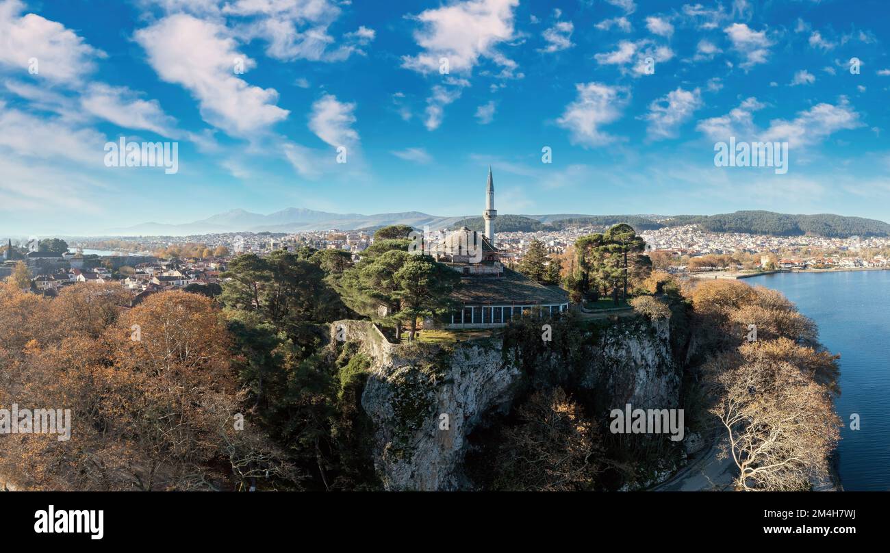 Greece, Ioannina Pamvotida Lake, Epirus. Aerial drone view of Giannena city and Aslan Pasha mosque on top of rocky hill, cloudy blue sky background. Stock Photo