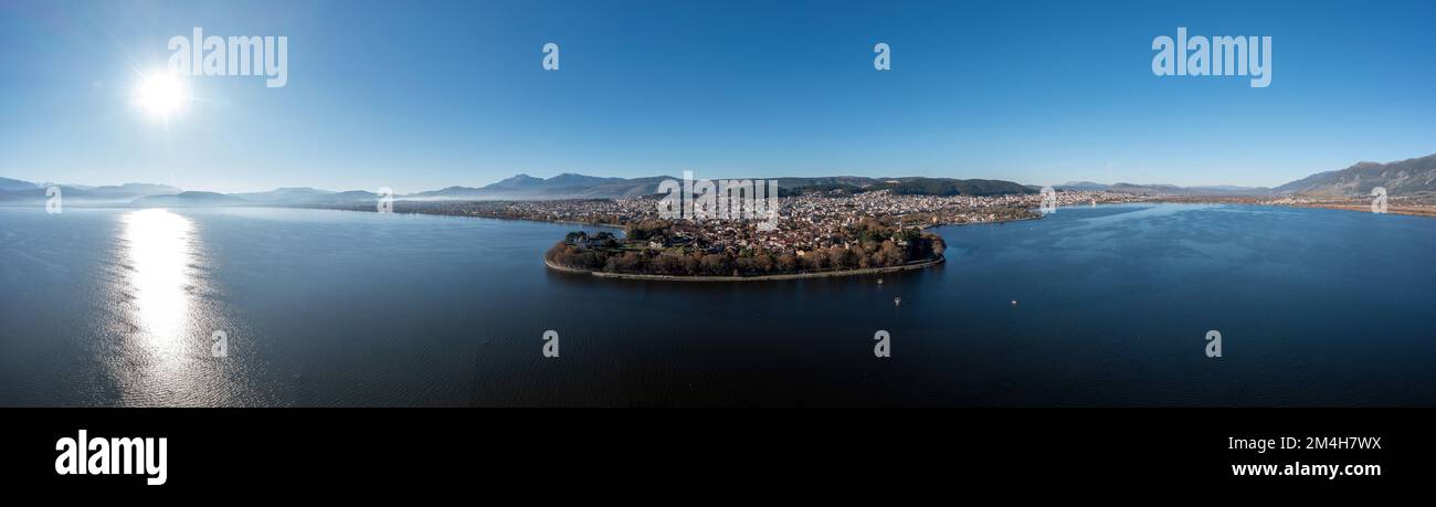 Greece, Ioannina city. Aerial panoramic drone view of Giannena town and Lake Pamvotis, sun shine over calm water, blue sky. Epirus. Stock Photo