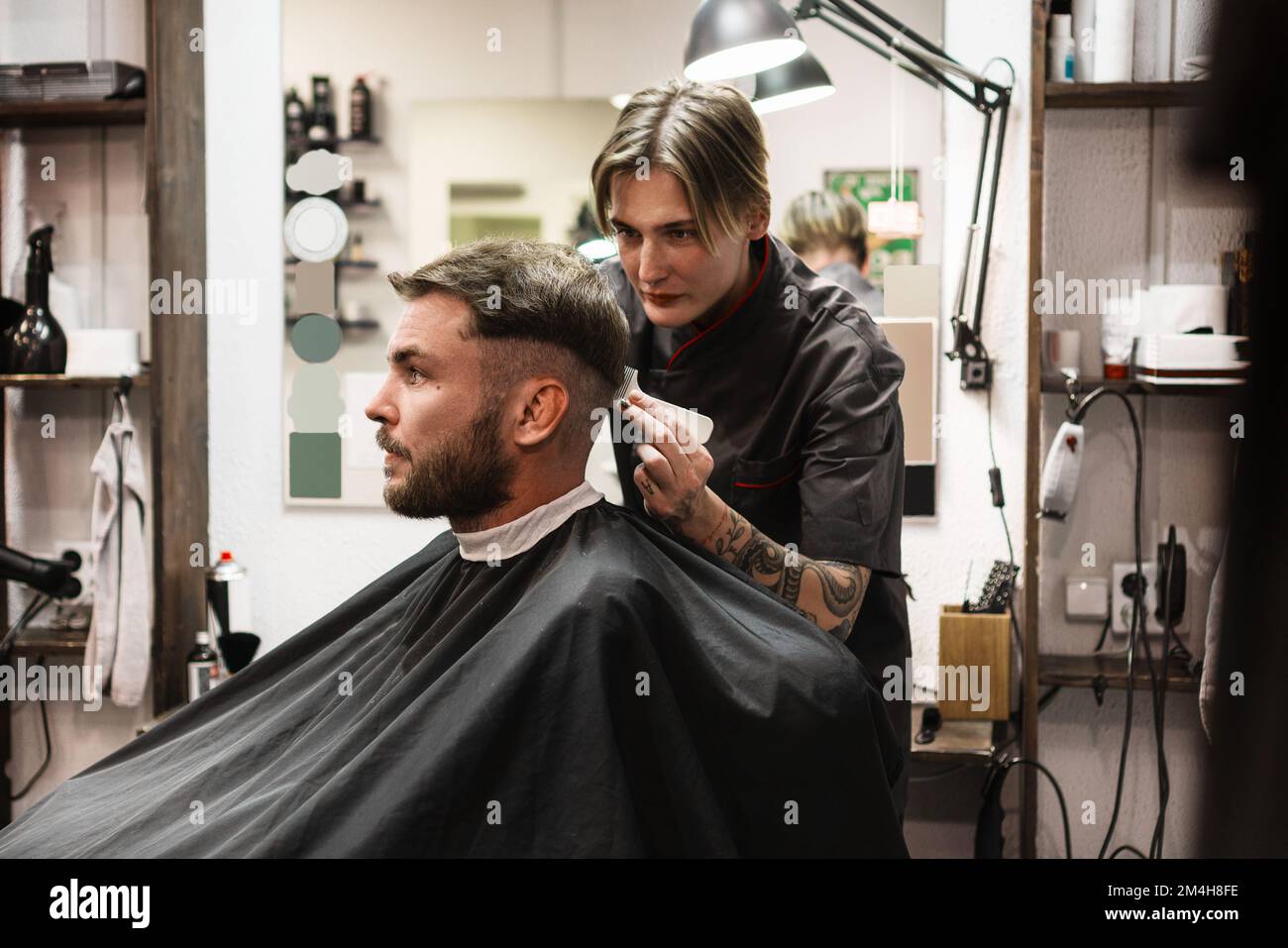 Man in barber shop, woman barber cutting hair to male with comb and scissors. Stock Photo