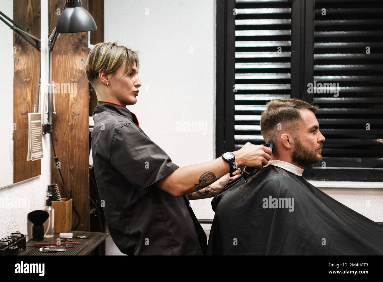 The barber woman cutting hair to man with trimmer in barbershop, real people, customer and hairdresser. Stock Photo