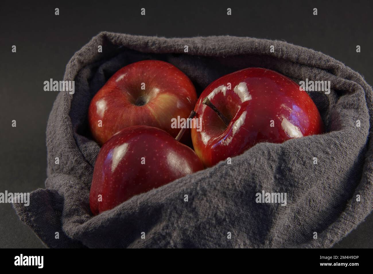 Three glosy delicious red apples in a gray basket against the dark background Stock Photo