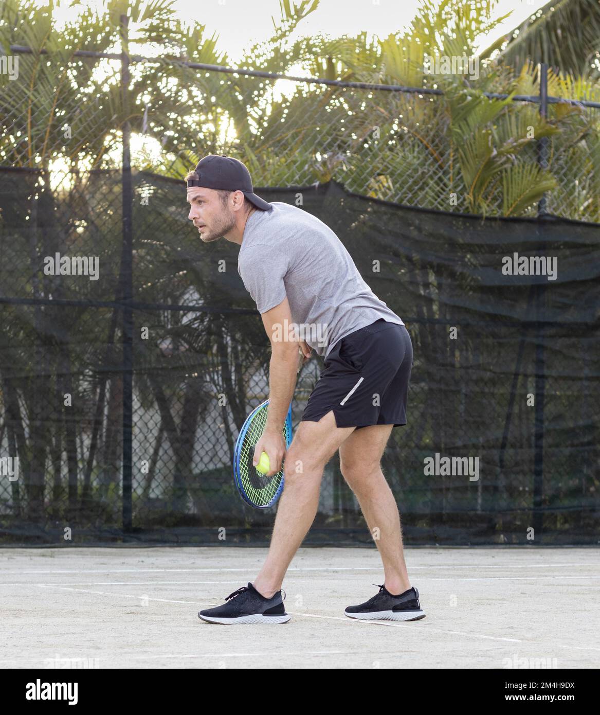 Young bearded man wearing cap plays tennis outdoors. Stock Photo
