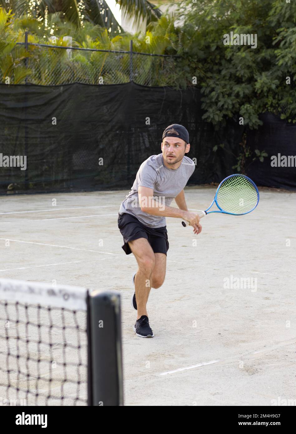 Young adult bearded man wearing cap plays tennis outdoors. Stock Photo