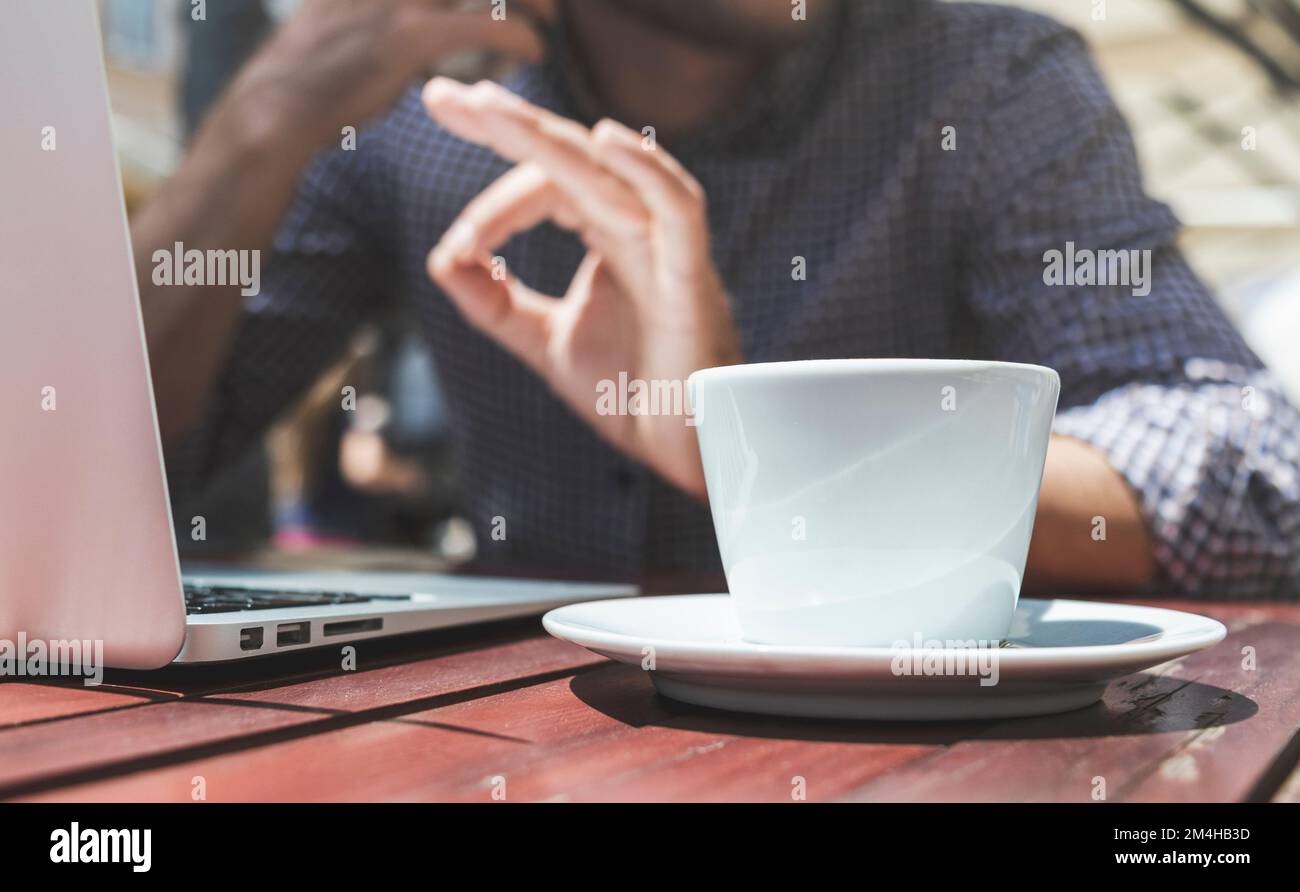 Cup of coffee on the table and defocused hand sign OK on background. Stock Photo