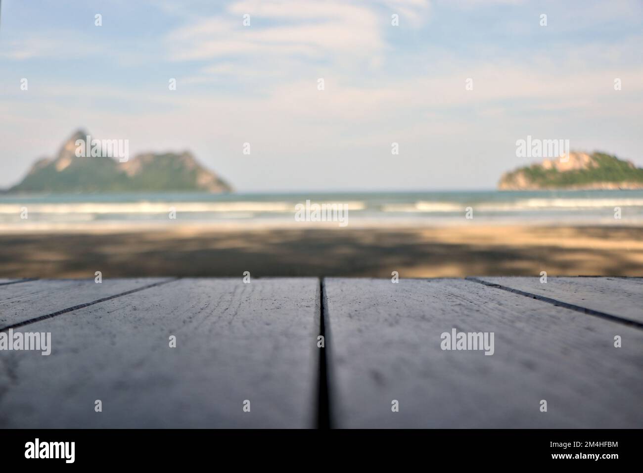 A wooden table on the sand with an island in the middle of the sea in the background. Stock Photo