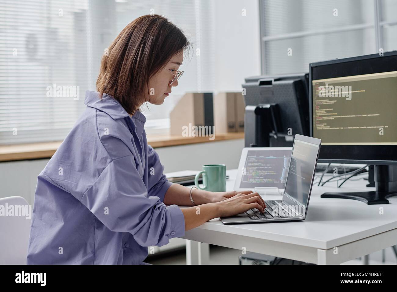 Asian young woman writing codes on laptop while working at her workplace in office Stock Photo