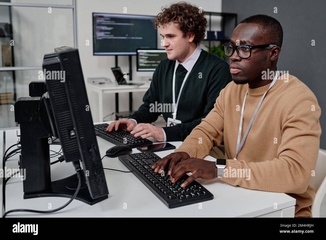 Two programmers sitting in front of computer monitors and writing security code for program Stock Photo