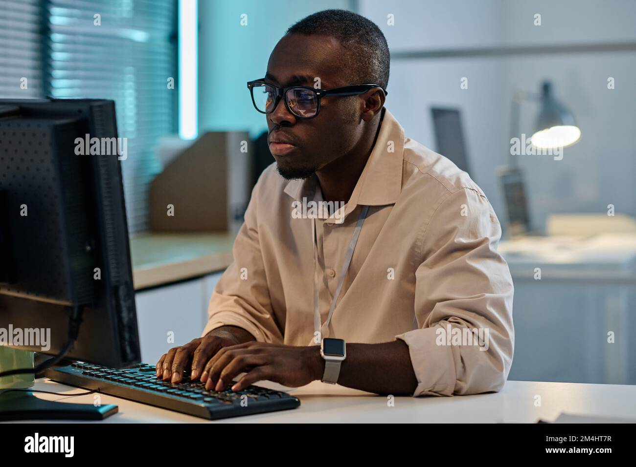 Serious African American programmer in eyeglasses typing on computer to develop new program, he working overtime in office Stock Photo