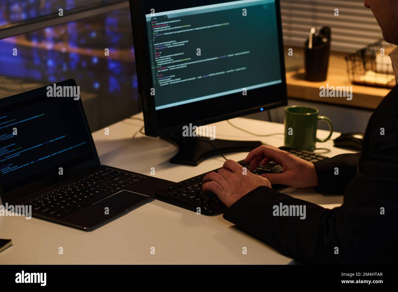 Close-up of programmer developing computer program with codes on computer while working in office till late evening Stock Photo