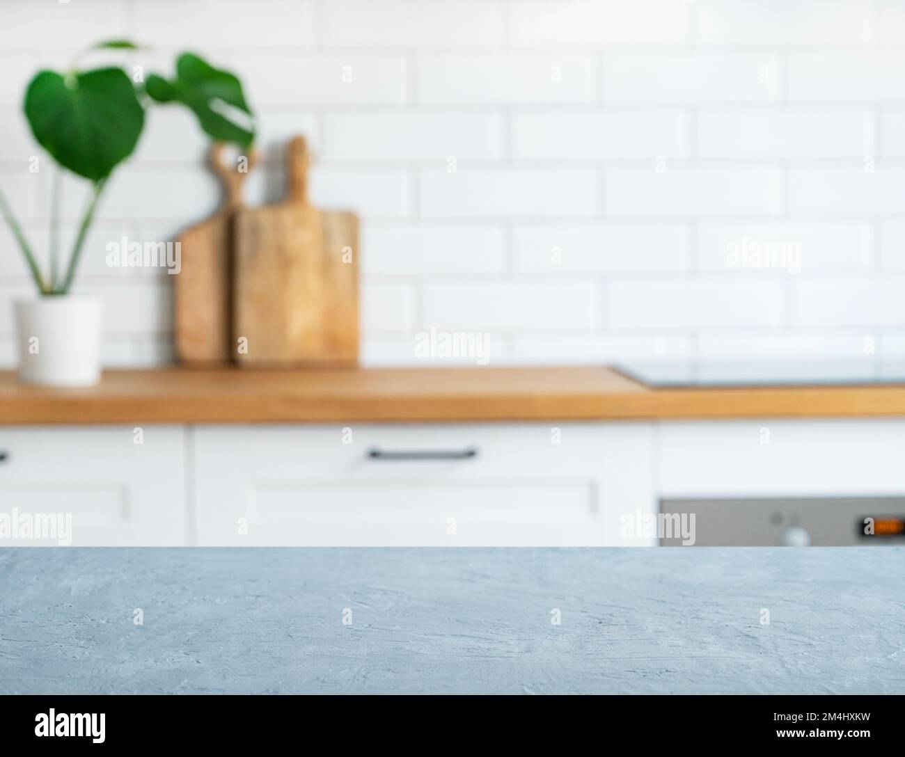 Wooden blue countertop with free space for mounting a product or layout against the background of a blurred white kitchen with cuting board and plant. Stock Photo
