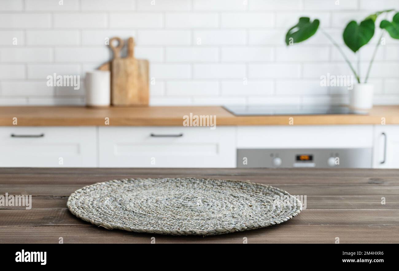 Dark wooden countertop with napkin and free space for mounting a product or layout against the background of a blurred white kitchen with plant. Horiz Stock Photo