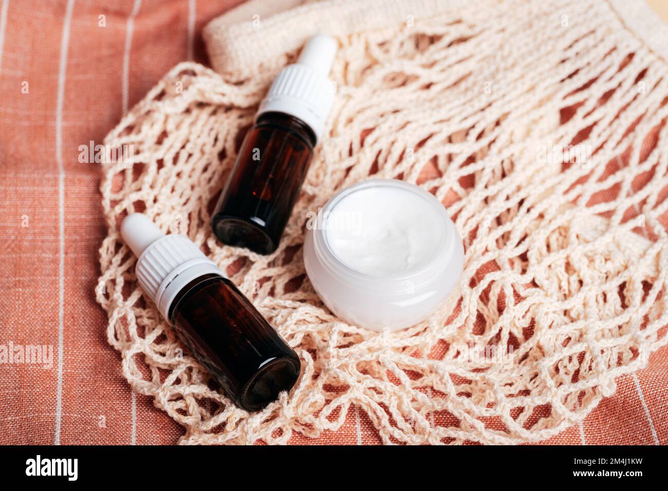 Cream jar and brown glass bottles with essential oils on mesh bag. Organic spa cosmetic beauty product. Zero waste concept. Top view Stock Photo