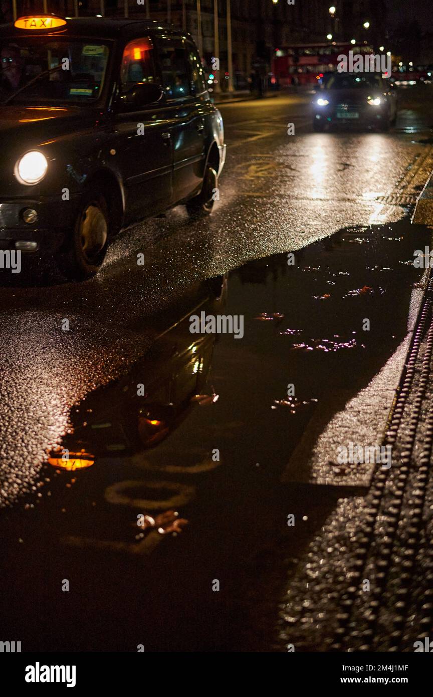 Blurred background with London black cab on wet road with large puddle Stock Photo