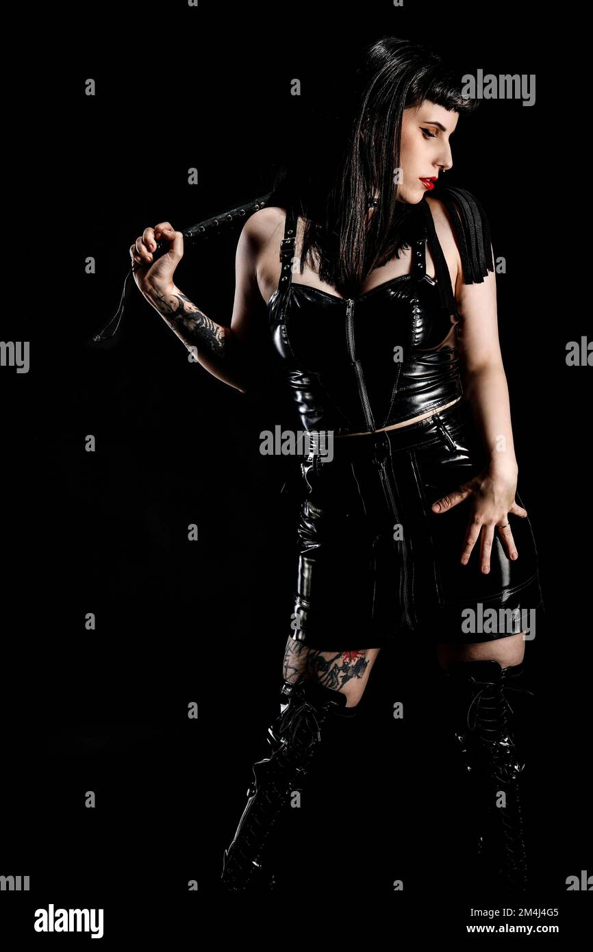 Woman with black hair and tattos in vinyl and latex outfit and whip, flogger,  BDSM Stock Photo - Alamy