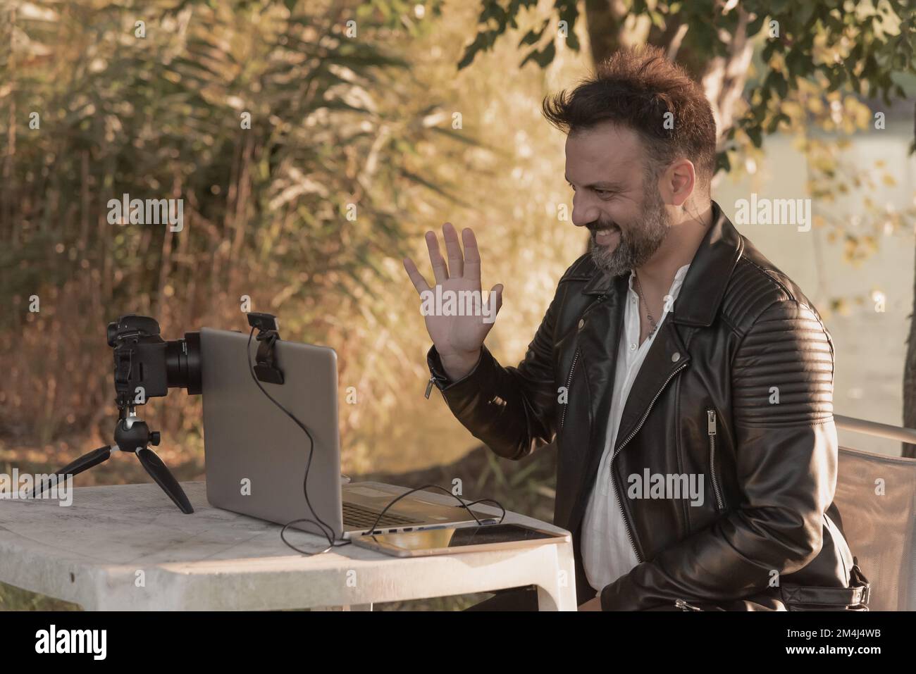 Man greeting through laptop webcam, connecting to the internet outdoors surrounded by nature at sunset Stock Photo