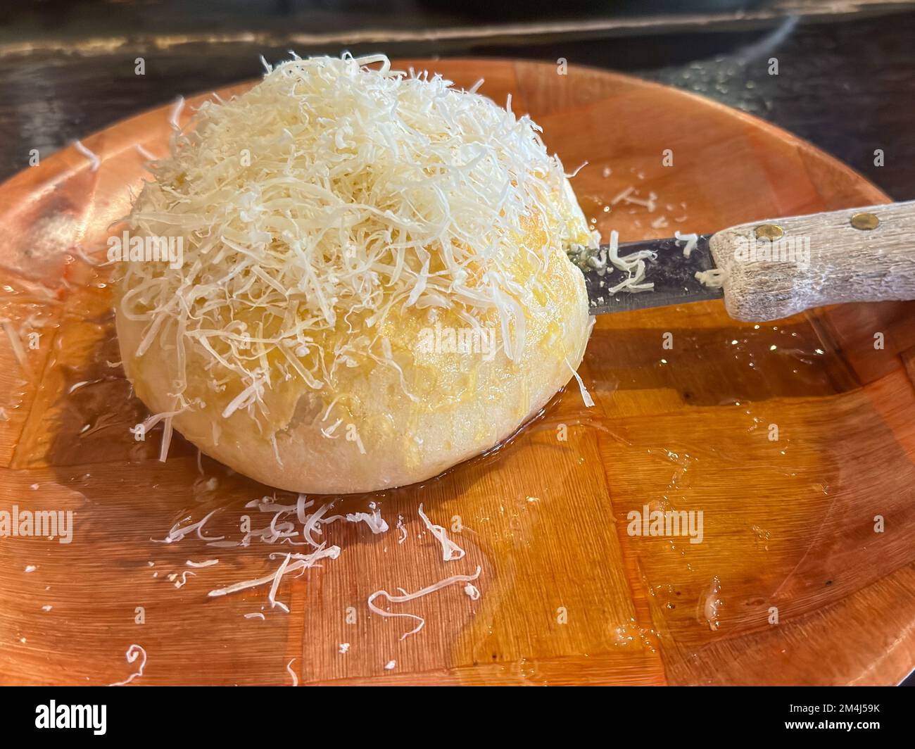 Delectable loaf of round bread covered in parmesan cheese sitting in a pool of melted butter on a plate. Stock Photo