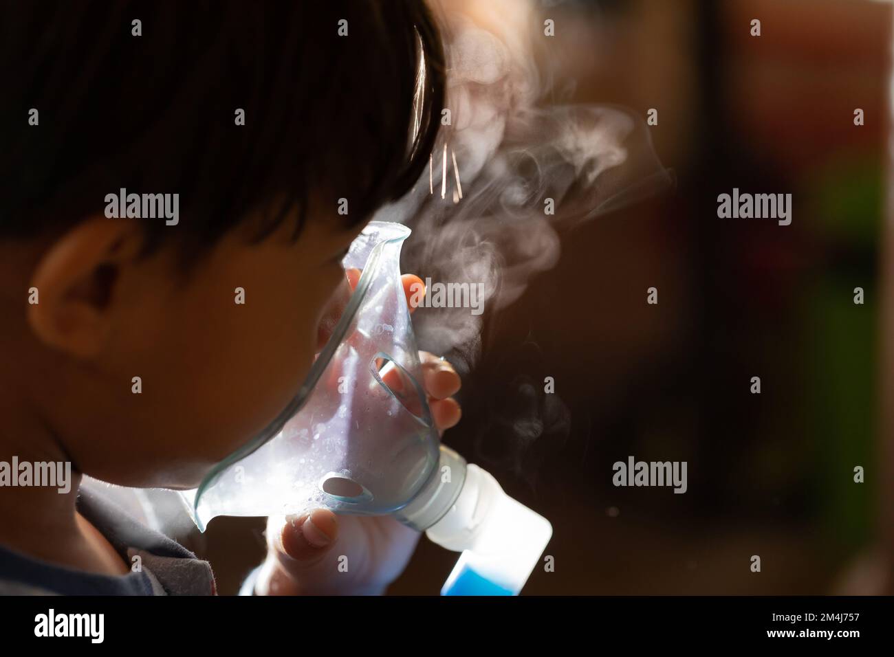 Portrait of a coughing child who is doing aerosol. Closeup of the nebulizer with the steam