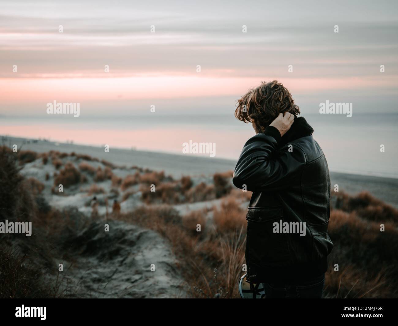 A young man wearing a black leather jacket and looking at the horizon at sunset Stock Photo