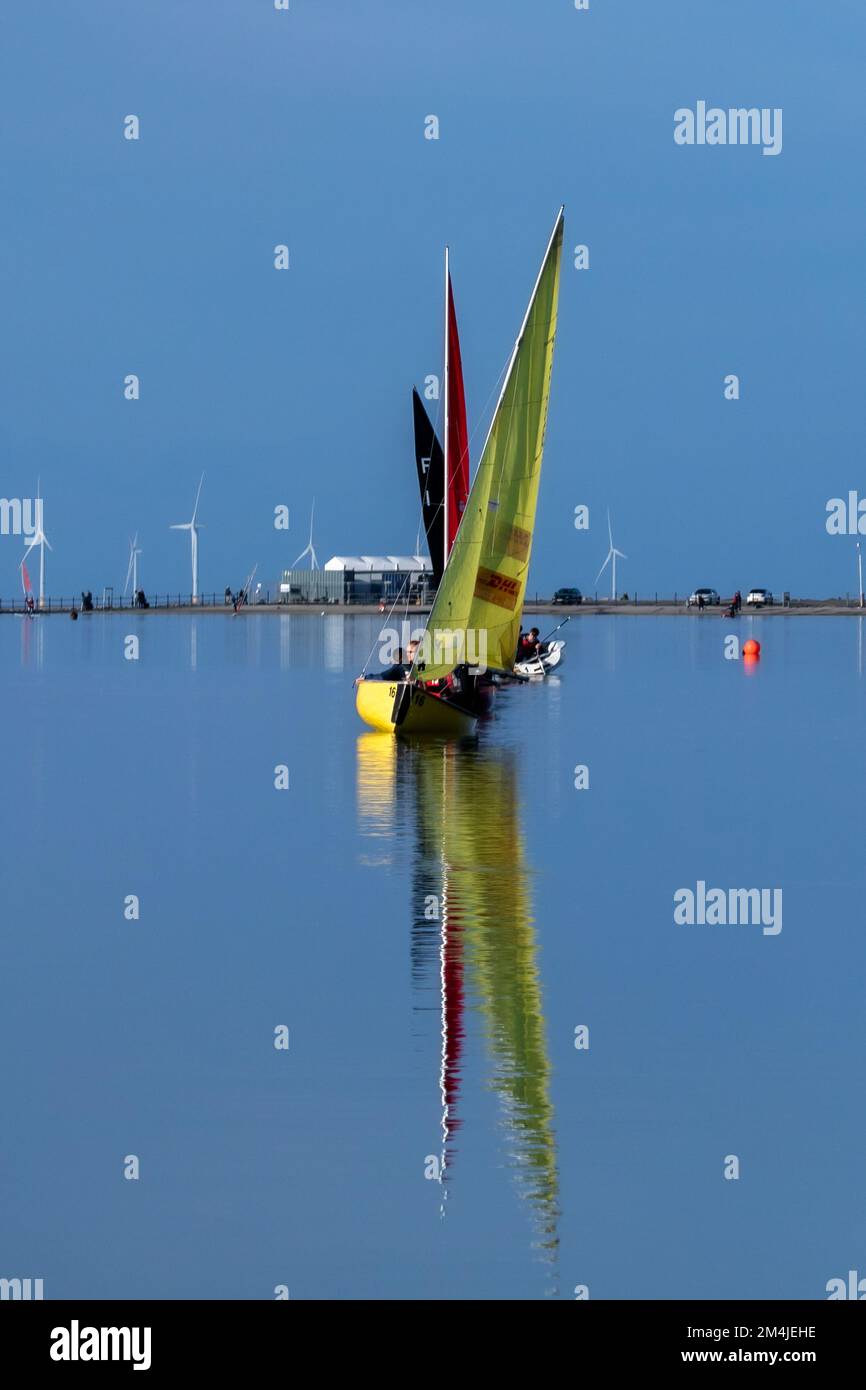 Colourful sailing dinghies from West Kirby Sailing Club reflected in calm waters of West Kirby marine lake, Wirral Stock Photo