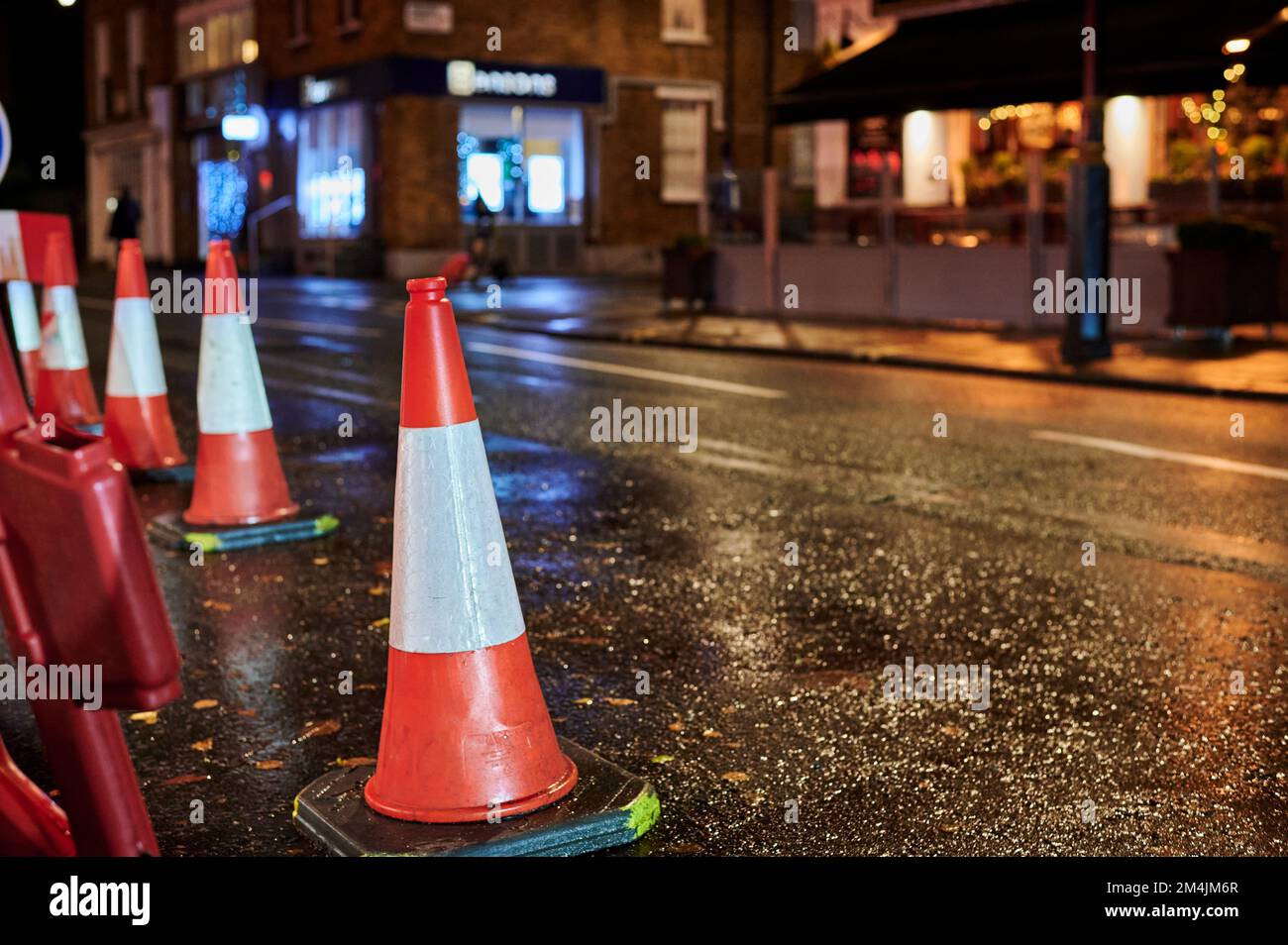 Low view of roadwork cones on wet street at night with blurred background Stock Photo