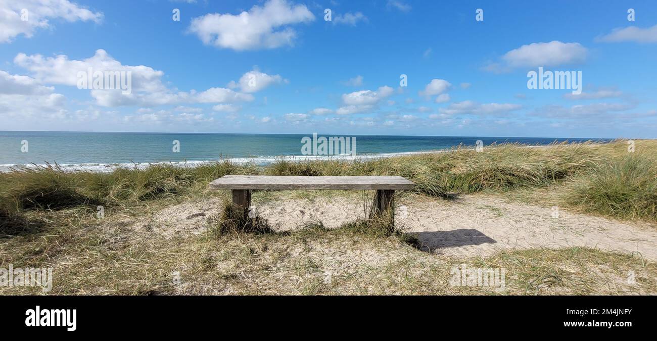 A panoramic shot of the sandy beach with a chair by the blue sea under ...