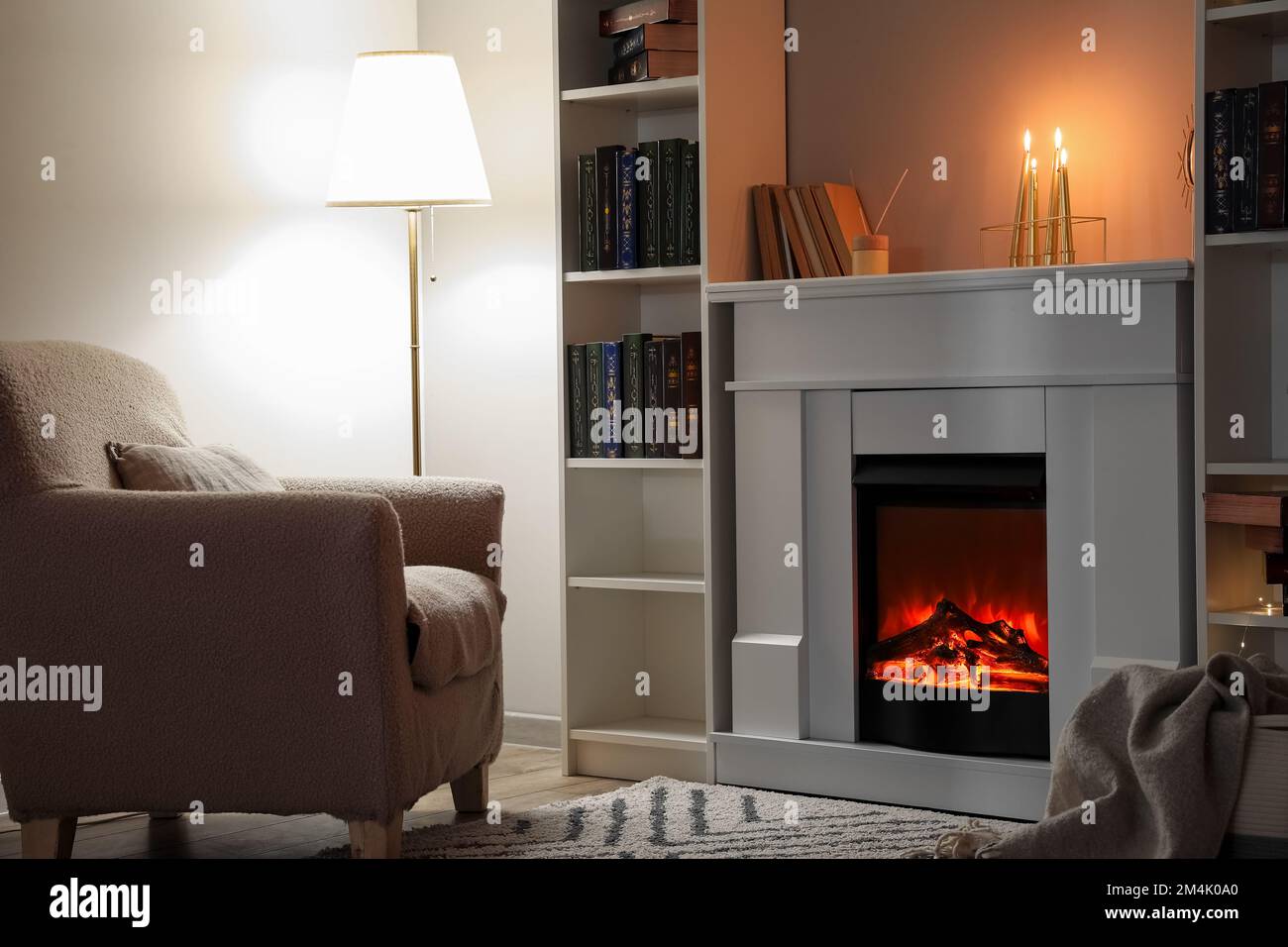Interior of living room with fireplace, burning candles and bookshelves