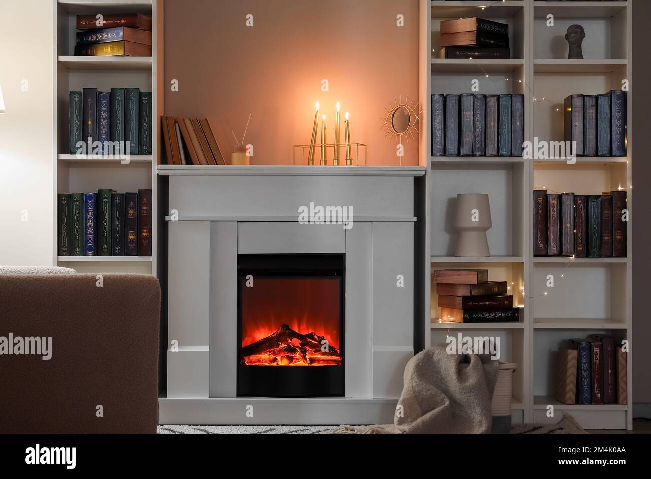 Interior of living room with fireplace, burning candles and bookshelves