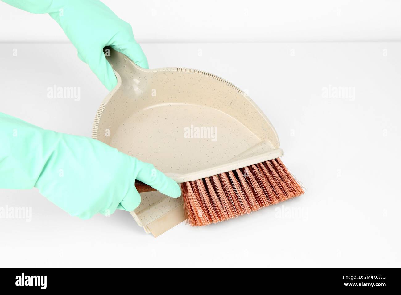 Female hands in rubber gloves with dustpan and brush on white