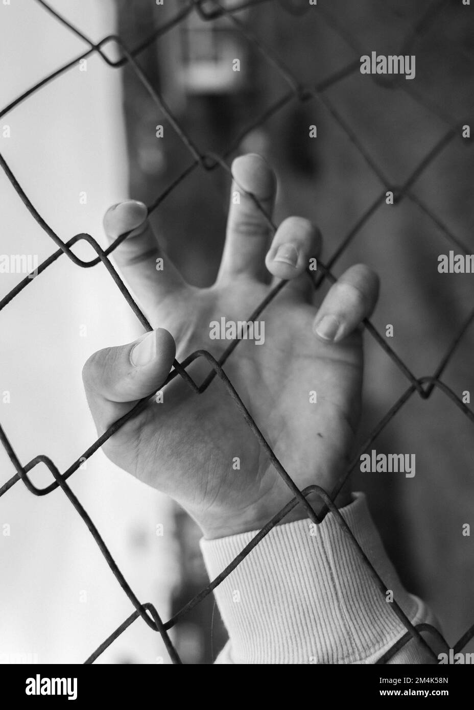 A grayscale of a hand holding a grid fence as a concept of freedom and peace Stock Photo