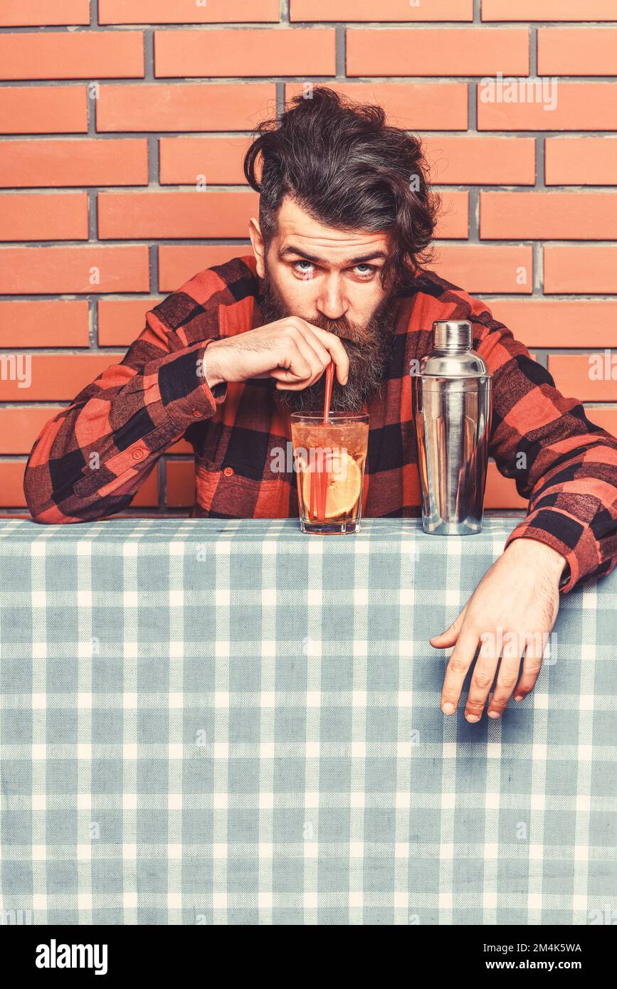 Man drinks cocktail on brick wall background. Alcohol and cocktails concept. Barman with beard and surprised face drinks out of glass with drinking Stock Photo