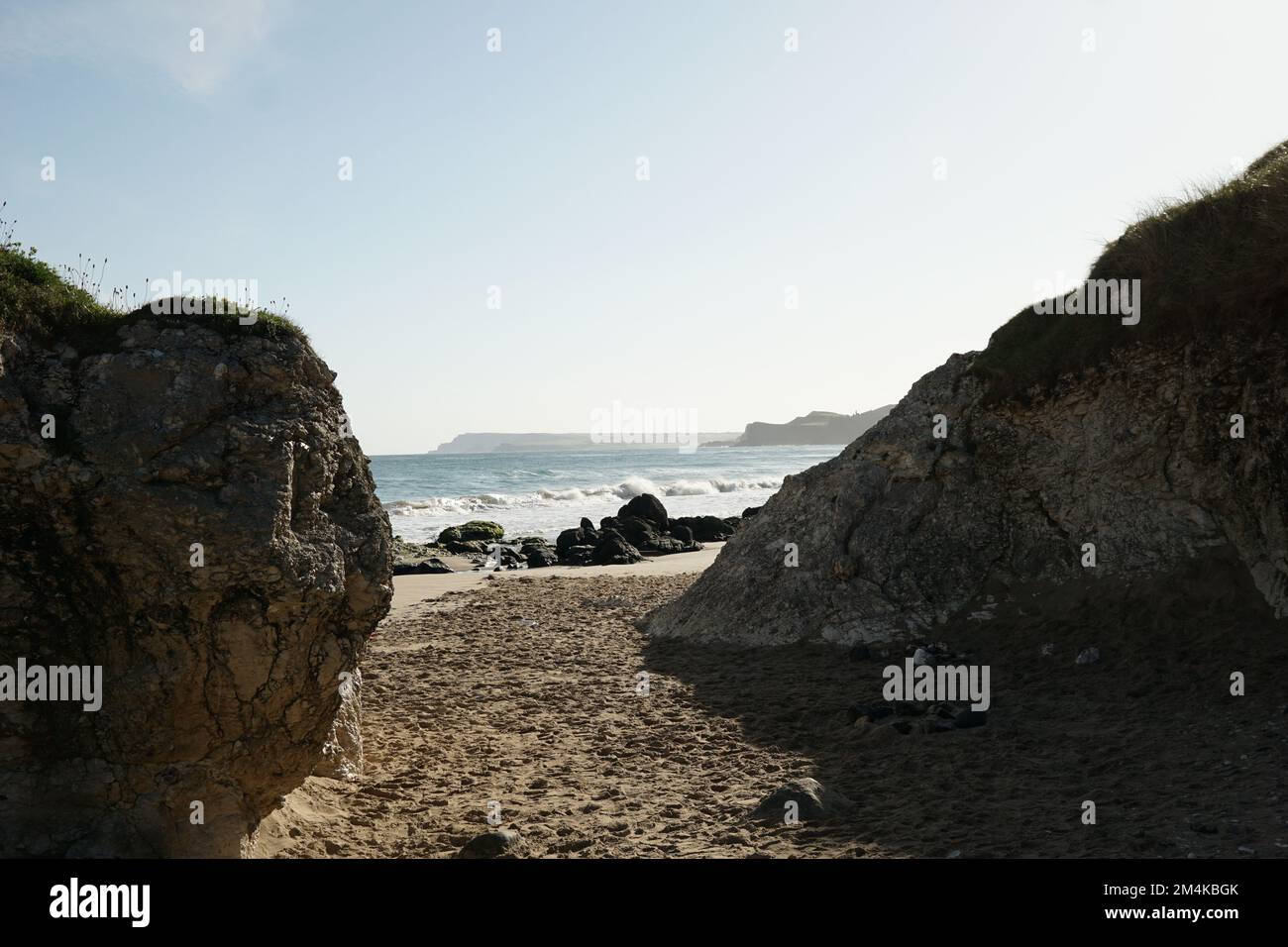 A sandy path amid the coastline hige rocks leading to the rocky beach ...