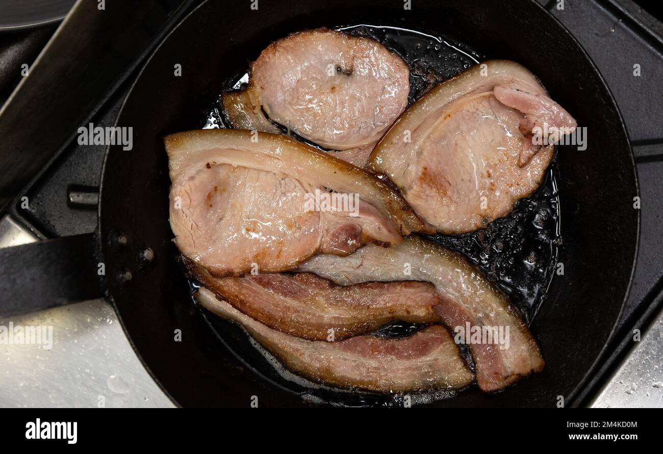 Thick cut bacon slices frying in cast iron pan Stock Photo