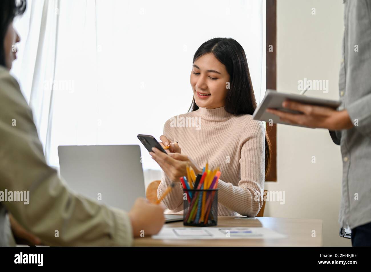 Professional millennial Asian female developers working with her colleagues on a new mobile application prototype. Stock Photo