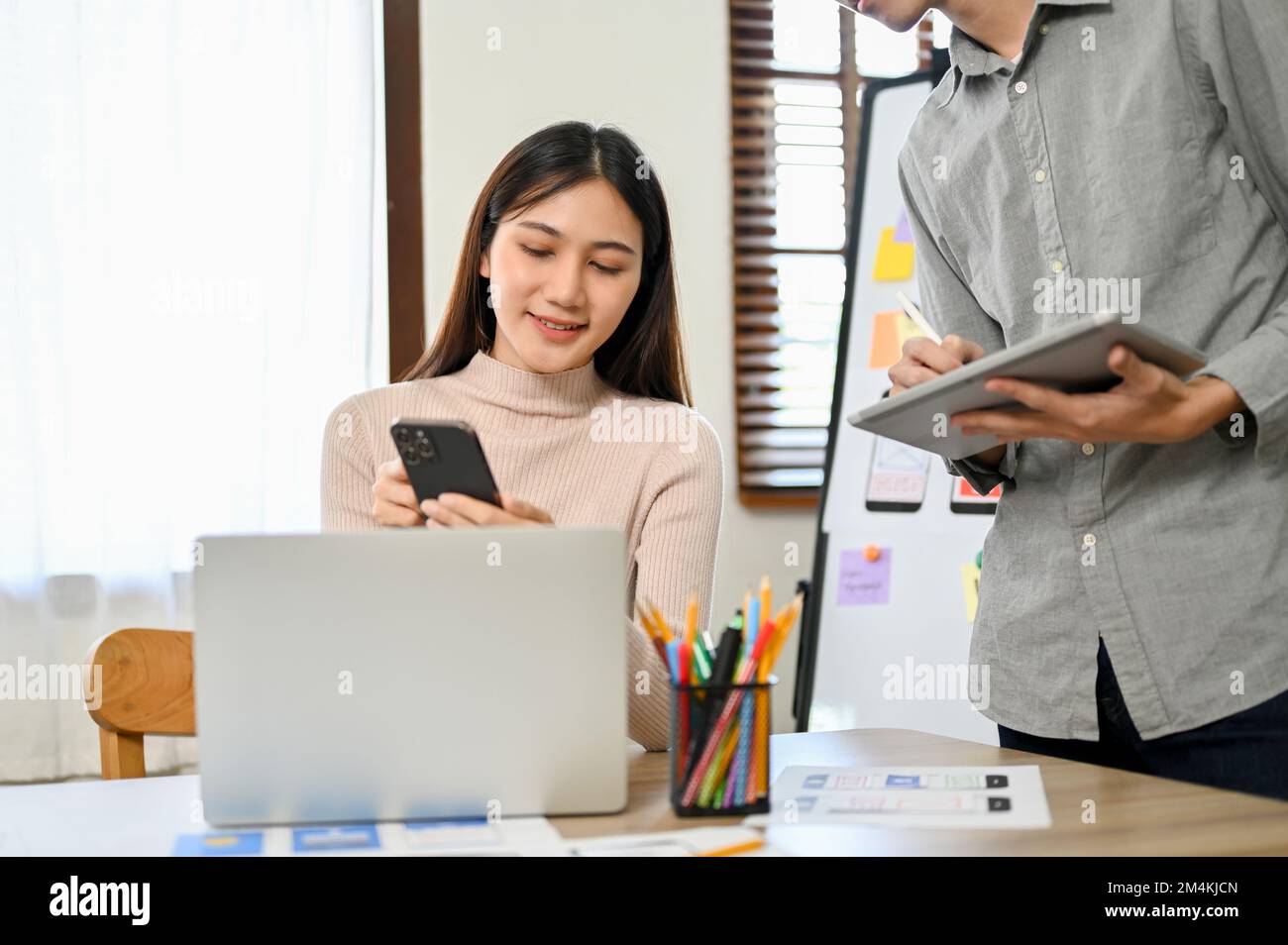 Professional millennial Asian female developers working with her colleague on a new mobile application prototype. UI UX business startup concept Stock Photo