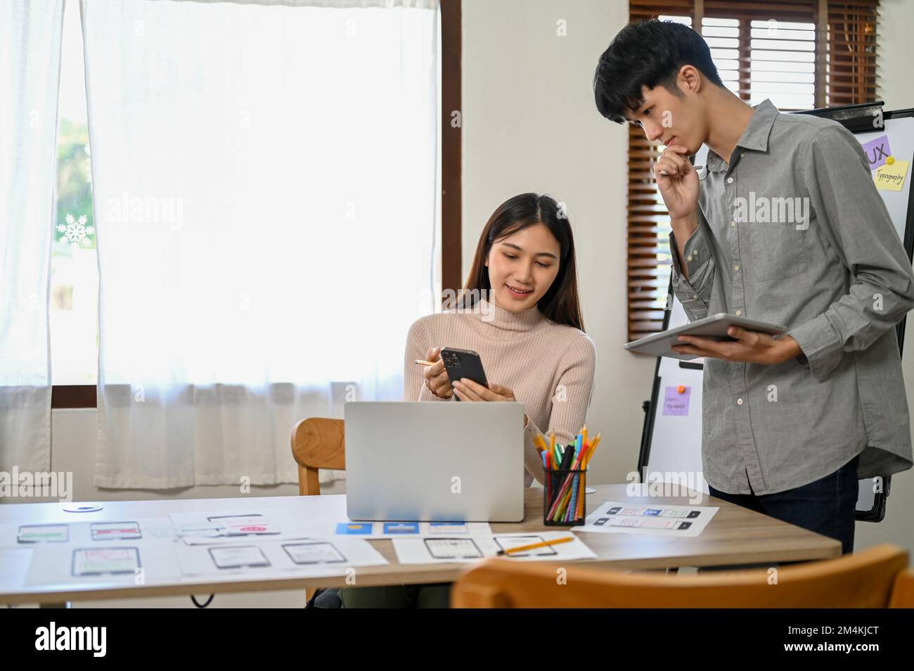 Professional millennial Asian male and female developers are in the meeting room, working together on their new mobile application prototype. UI UX bu Stock Photo