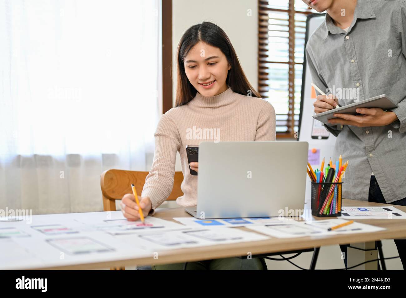 Attractive and professional millennial Asian male and female developers are in the meeting room, working together on their new mobile application prot Stock Photo