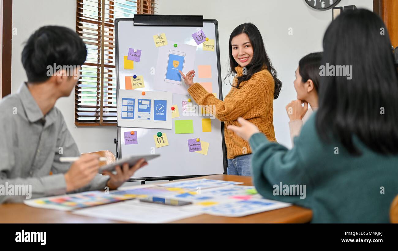 Professional millennial Asian female graphic designer presenting her new prototype of her new mobile application to her team in the meeting. UX UI sta Stock Photo