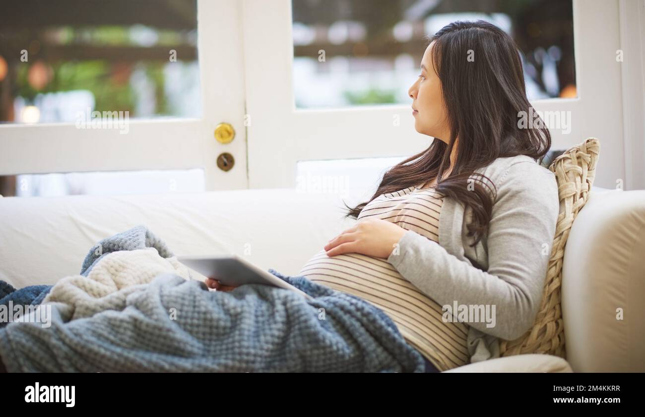 The big day is nearly here. a pregnant woman looking thoughtful while using a digital tablet at home. Stock Photo
