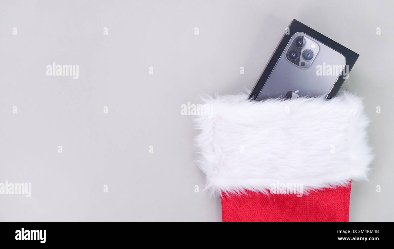 iPhone gift box looking out of Christmas socks. Santa's red stocking full of gifts. Concept of christmas or holiday. Gifts on grey background. Gatinea Stock Photo